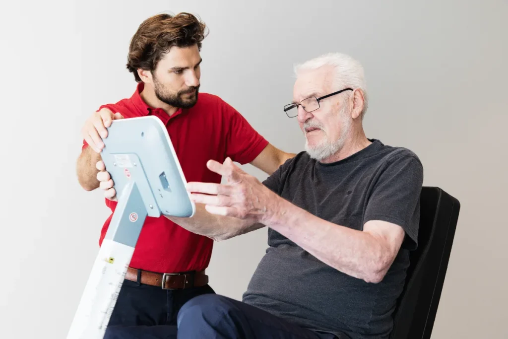 Ergotherapeut erklärt einem älteren Patienten eine Übung – PhysioVital Hamburg-Bramfeld